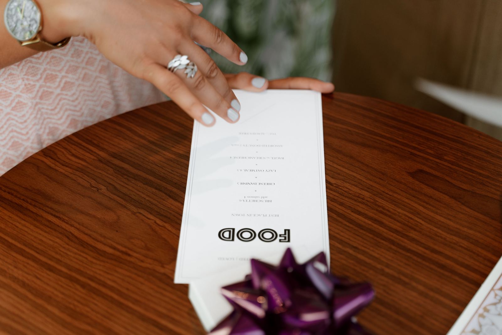 A guest's hand holding an open printed restaurant menu over a wooden table